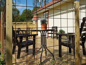 A wooden deck with metal fencing, outdoor furniture, and a building with a red roof in the background. - 5 Person Holiday Home in Hunnebostrand (Hunnebostrand)