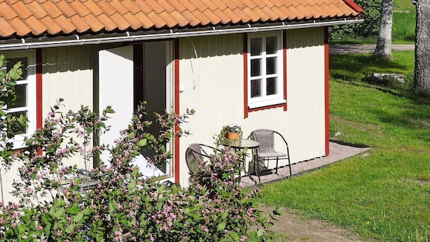 A single-story building with a tiled roof, a door, and a window. There is a chair and a table outside. - 5 Person Holiday Home in Hunnebostrand (Hunnebostrand)