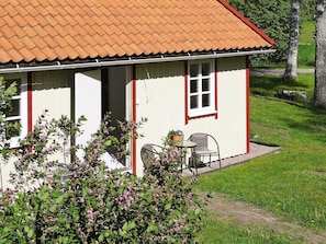 A single-story building with a tiled roof, a door, and a window. There is a chair and a table outside. - 5 Person Holiday Home in Hunnebostrand (Hunnebostrand)