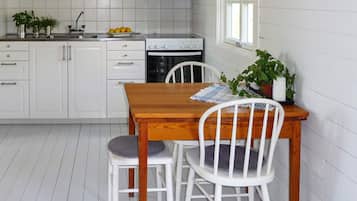 A kitchen with white cabinets, a wooden table, two white chairs, and a window.