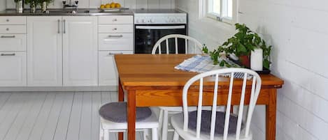 A kitchen with white cabinets, a wooden table, two white chairs, and a window.