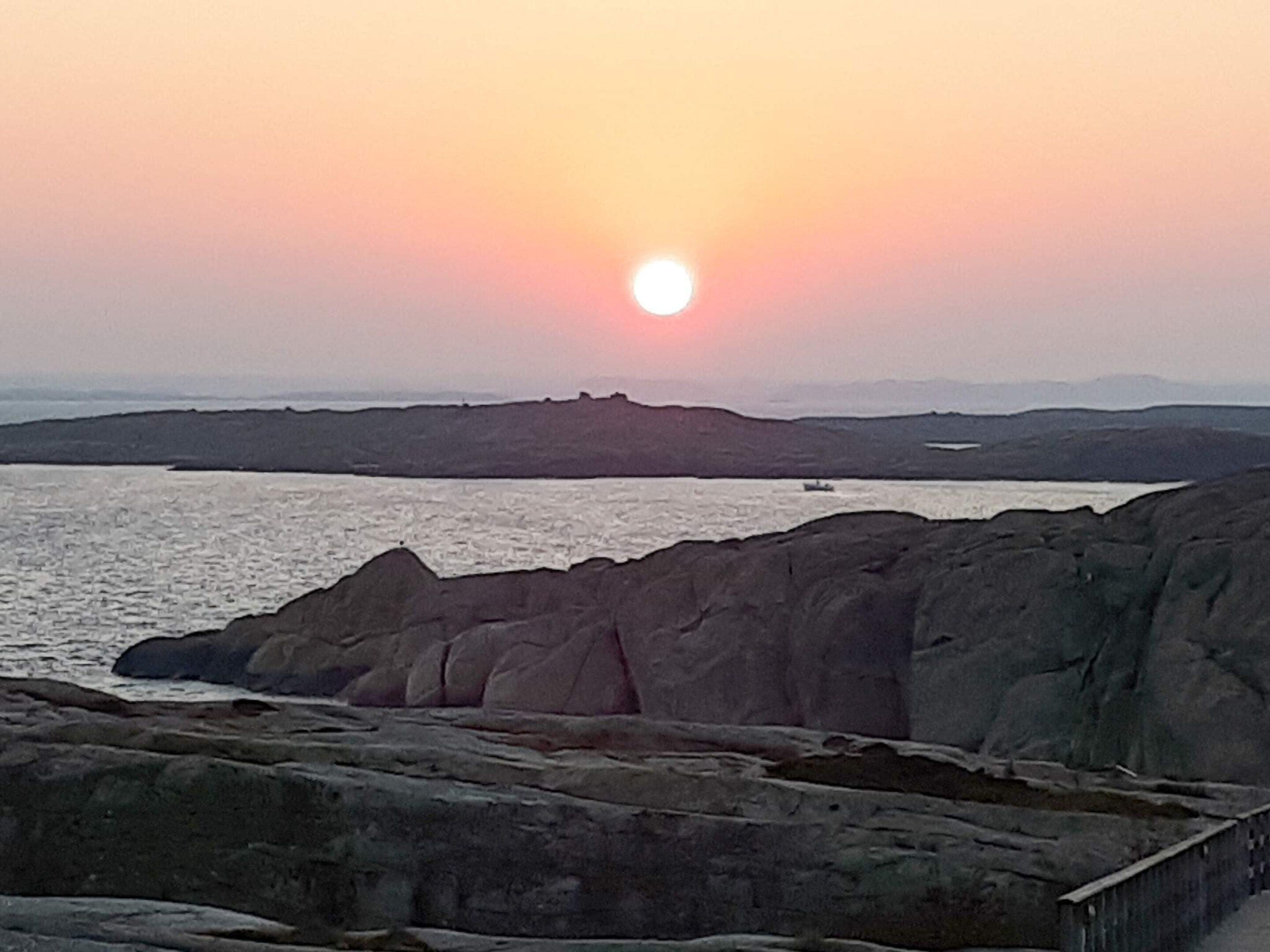 A coastal landscape with a sunset, rocky terrain, and a distant body of water.