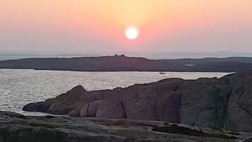 A coastal landscape with a sunset, rocky terrain, and a distant body of water.
