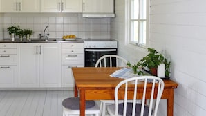 A kitchen with white cabinets, a wooden table, two white chairs, and a window. - 5 Person Holiday Home in Hunnebostrand (Hunnebostrand)