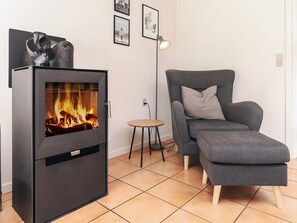 A modern living room with a wood-burning stove, a grey sofa, a small round table, and framed pictures on the wall.