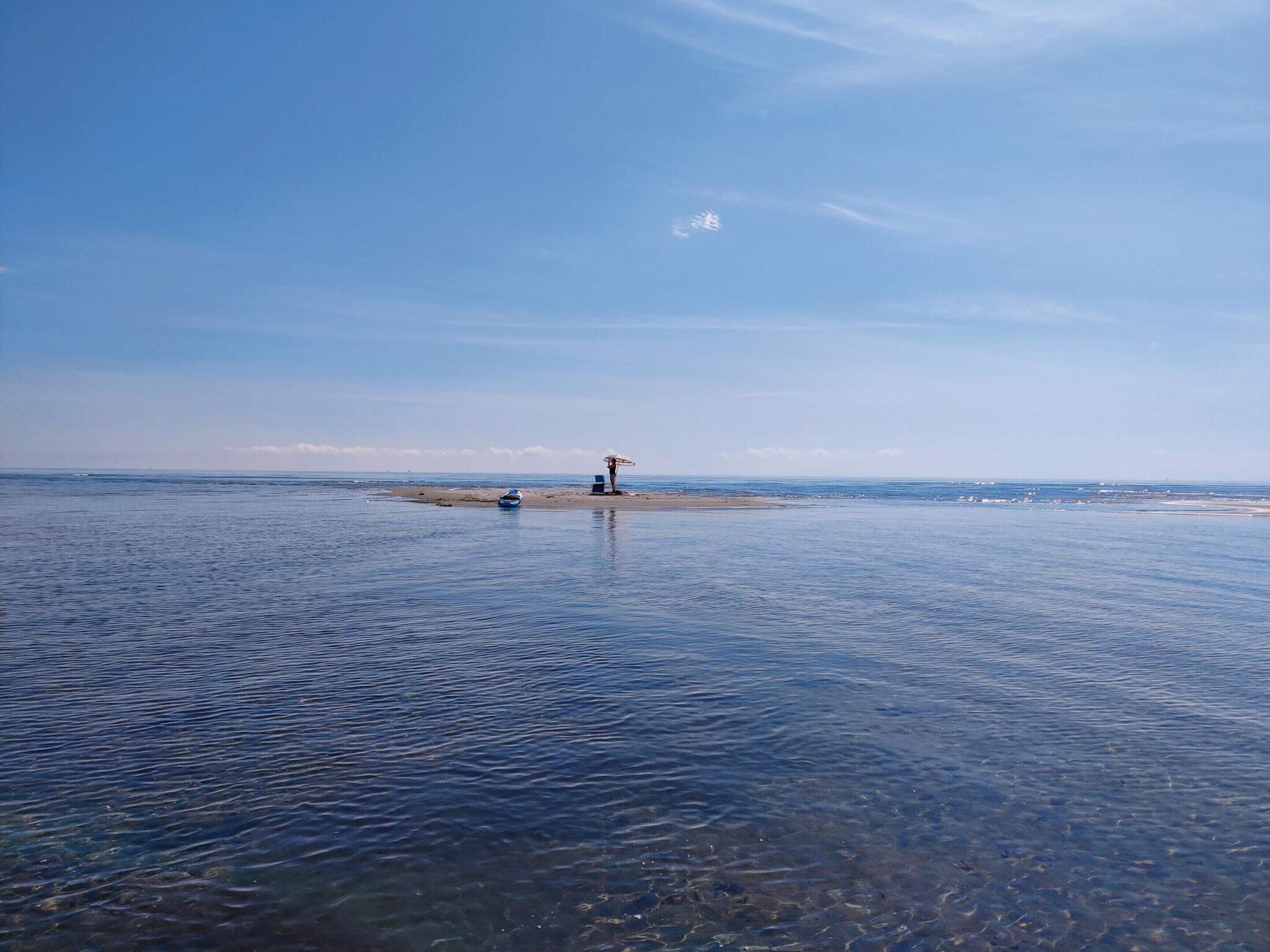 Une plage avec une eau cristalline, un petit bateau et un parasol de plage.