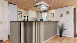 A modern kitchen with a wooden ceiling, a built-in island with a black and white striped countertop, and white cabinets. - 5 Star Holiday Home in Hals (Asaa)