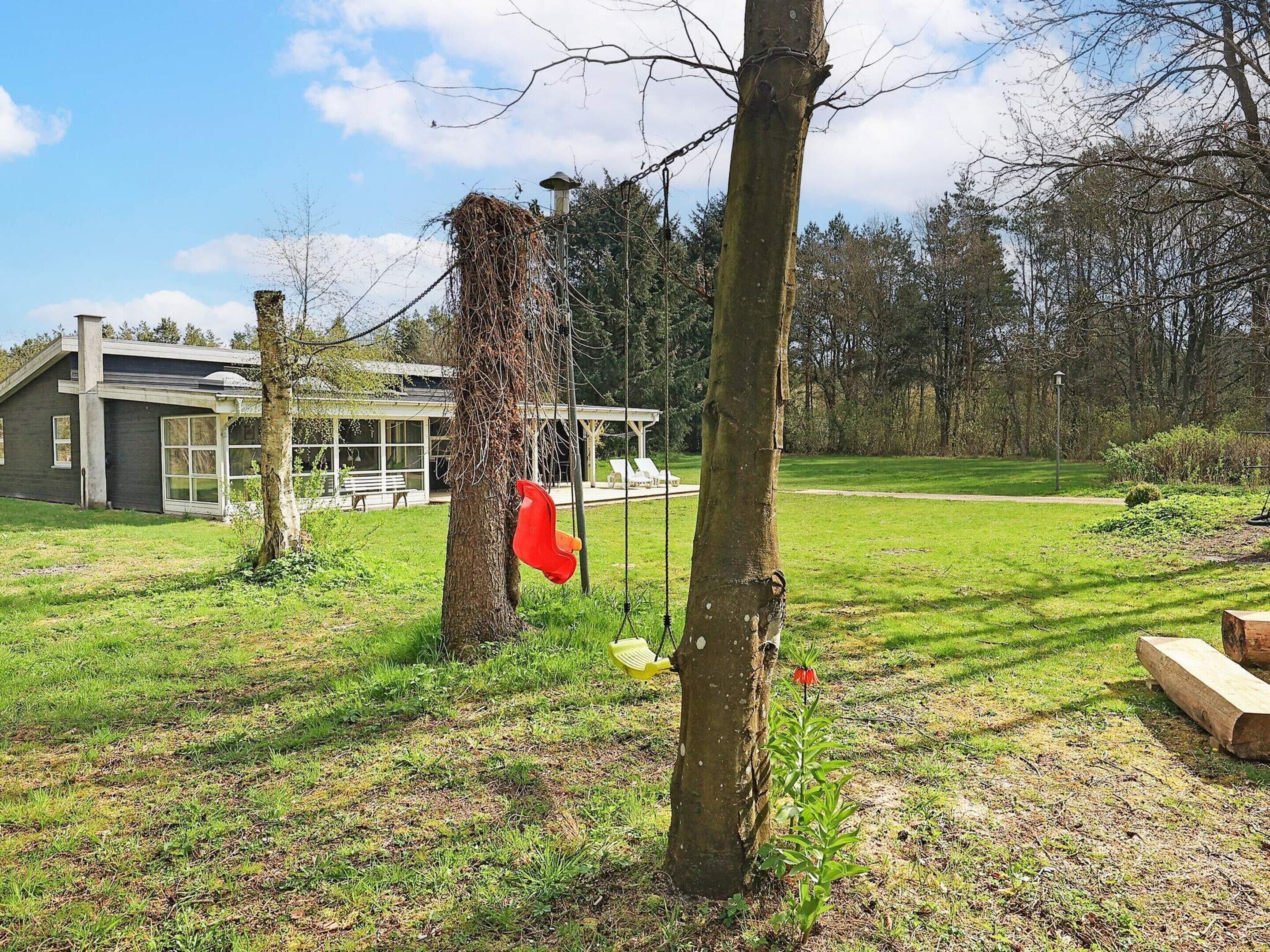A modern house with a large glass window, a grassy yard, and a tree with a red object attached to it.