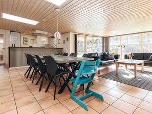 A spacious dining area with a long table and chairs, a kitchen area with a counter, and a living area with a sofa and coffee table.