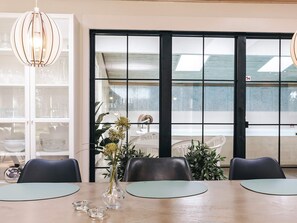 Un comedor con una mesa de madera, dos sillas, un florero con flores y un ventanal con vistas al exterior.