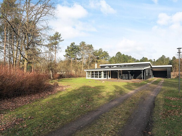 Un bâtiment moderne doté d’un garage, d’un espace extérieur couvert aménagé en coin salon et d’un chemin menant à cet espace.