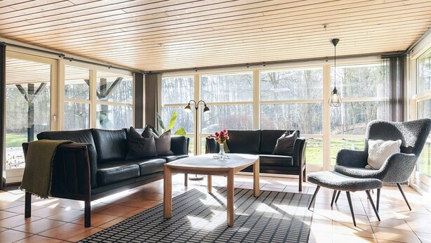 A spacious living room with a wooden ceiling, large windows, a black leather sofa, a coffee table, and a patterned rug. - 5 Star Holiday Home in Hals (Asaa)