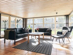 Un salon spacieux avec un plafond en bois, de grandes fenêtres, un canapé en cuir noir, une table basse et un tapis à motifs.