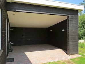 A garage with a dark exterior and a light interior, featuring a brick floor and a metal door. - 5 Star Holiday Home in Hals (Asaa)