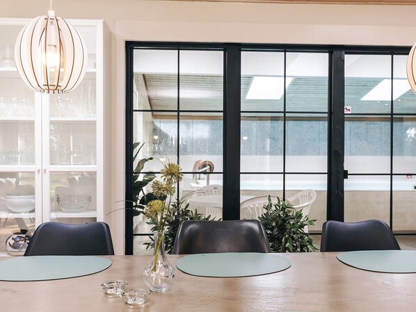 Un comedor con una mesa, sillas, un florero con flores y vistas amplias por las ventanas.