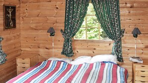 A wooden cabin room with a bed, two nightstands, a window with curtains, and a wall-mounted lamp. - 5 Person Holiday Home in Brekke-by Traum (Gulen)