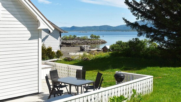 Ein Haus mit einer Terrasse, das auf einen See und Berge blickt.