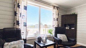 Ein Wohnzimmer mit zwei Ledersesseln, einem kleinen Tisch mit einer Dekoration und Blick ins Freie durch ein großes Fenster.
