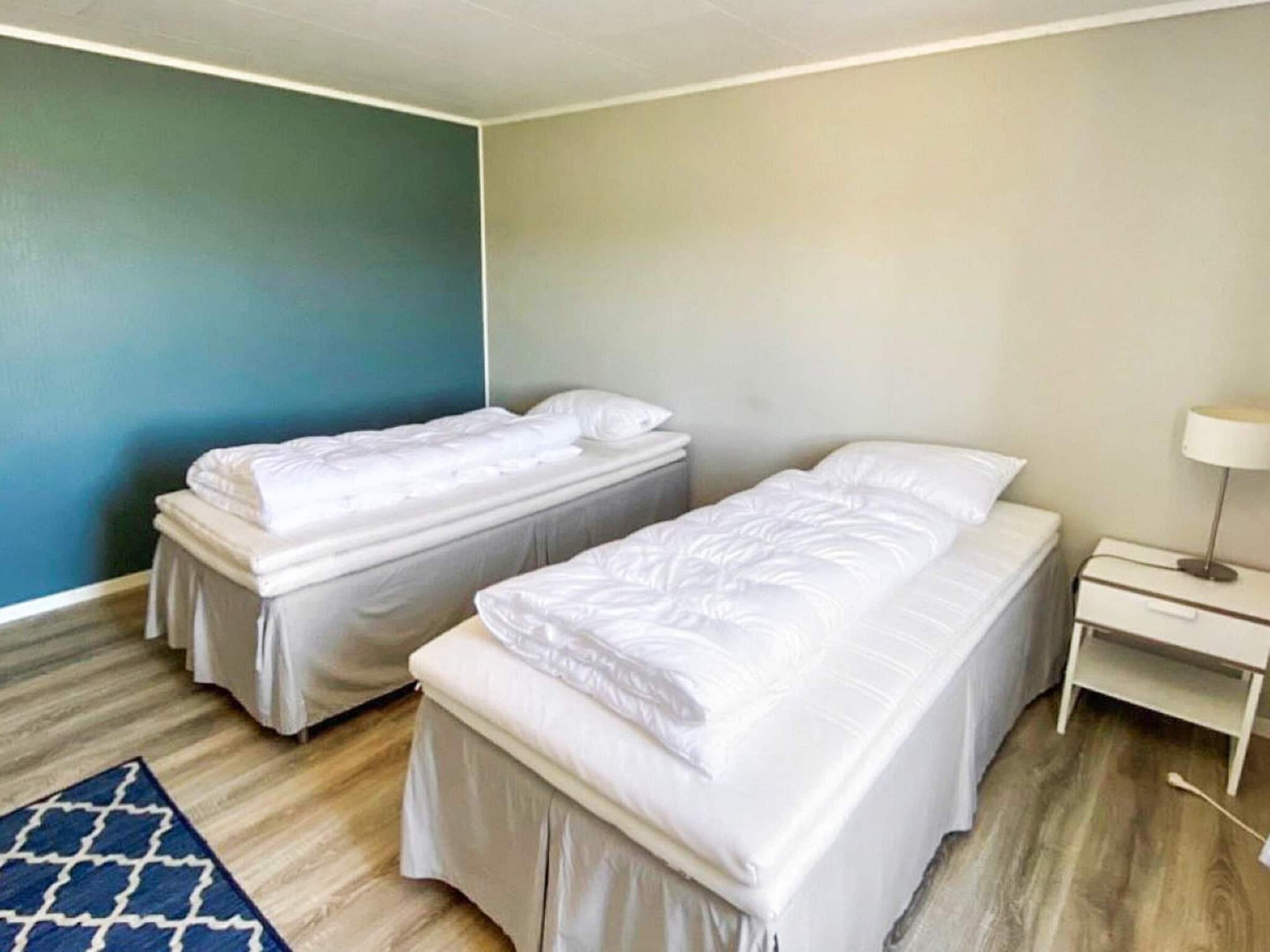 A room with two single beds, a bedside table with a lamp, and a blue accent wall.