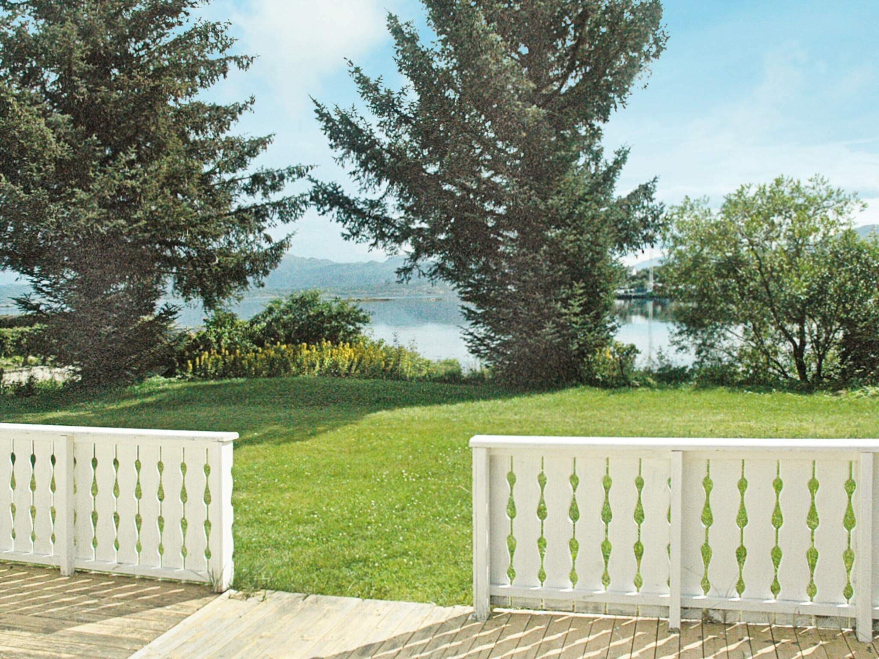 A deck with white balustrades overlooking a grassy area with trees and a lake.
