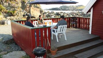 A wooden deck with a red railing, a barbecue grill, and a table with chairs under a blue umbrella.