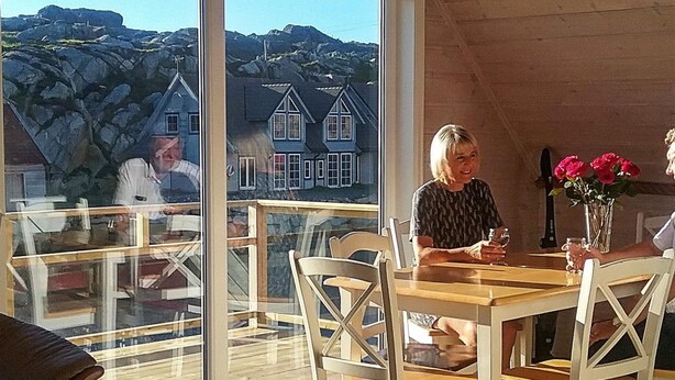 Uma área de refeições com mesa e cadeiras de madeira, grandes janelas com vista para casas e montanhas.