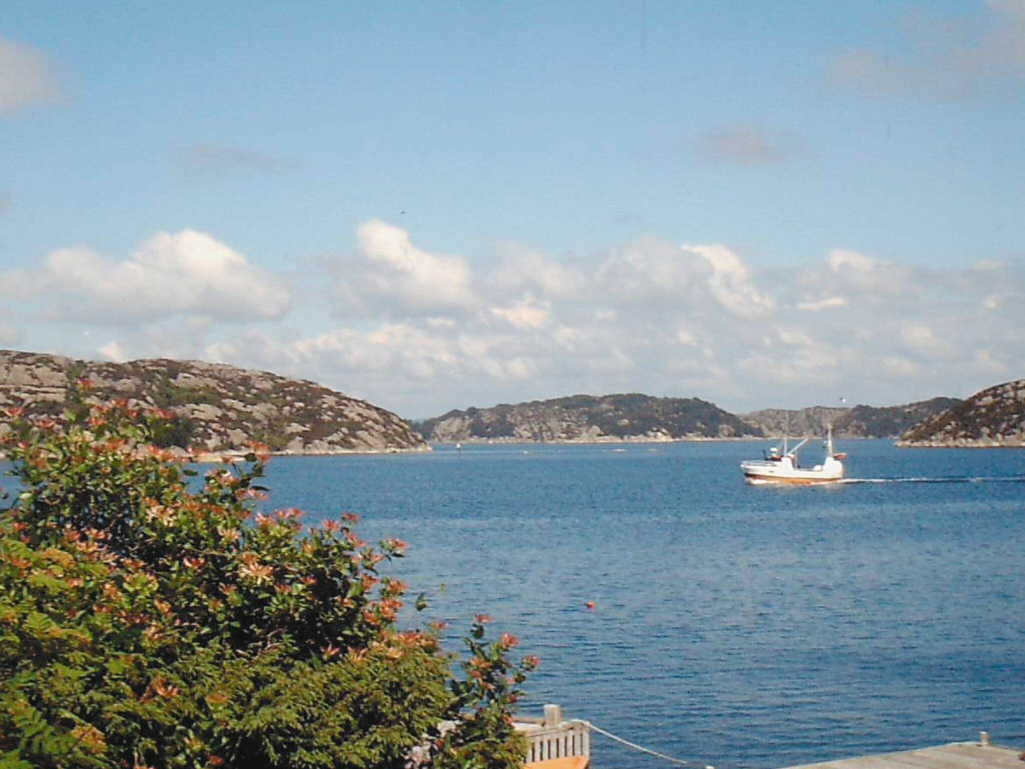 A coastal scene with a boat on the water and rocky hills in the background.