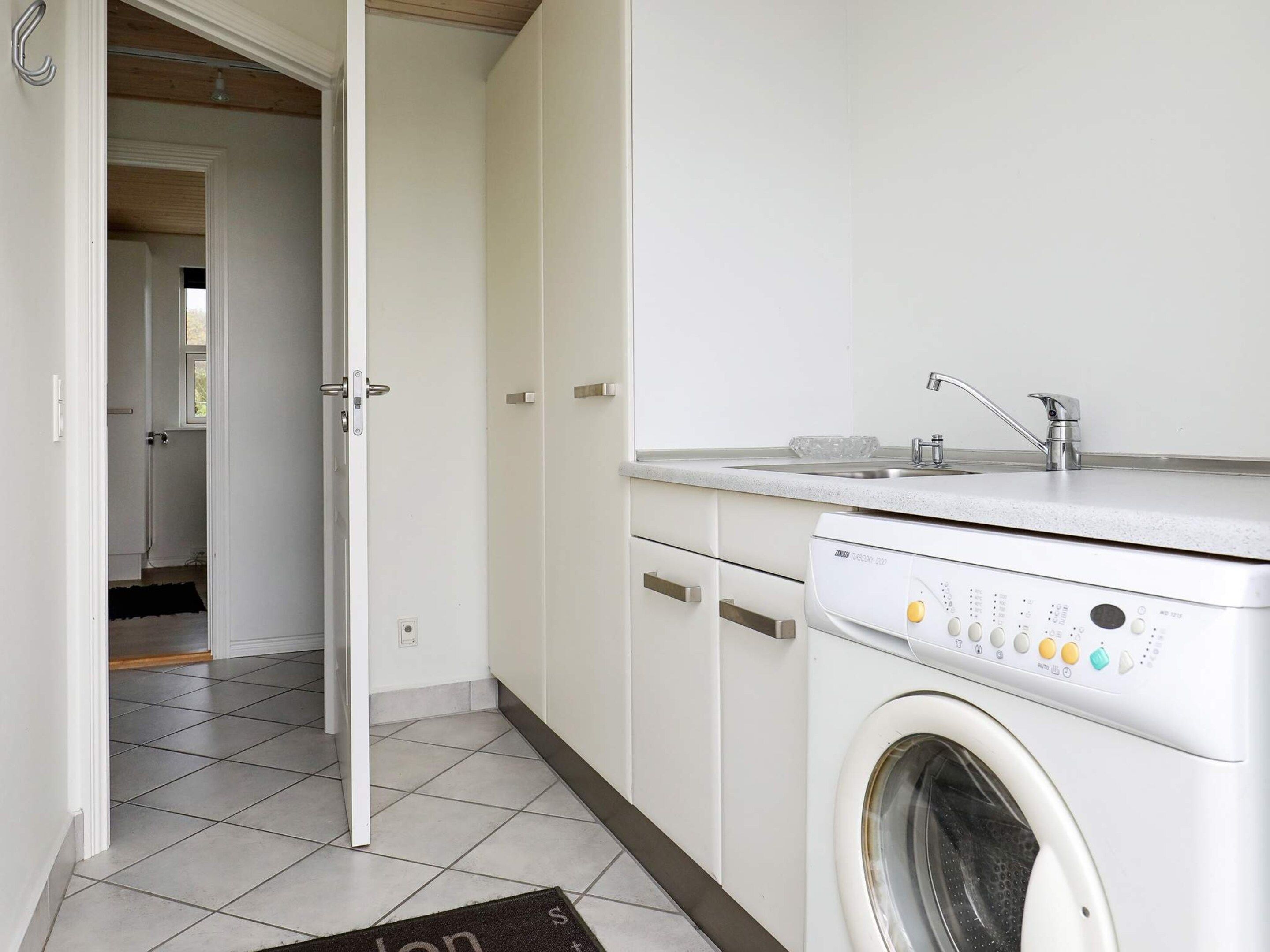 A laundry room with a front-loading washing machine, a sink, and cabinets.