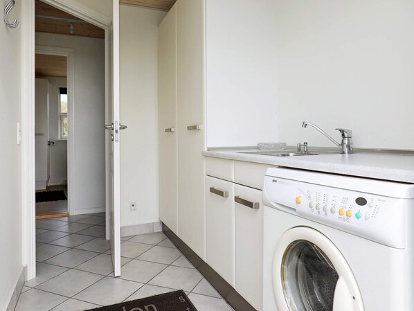 A laundry room with a front-loading washing machine, a sink, and cabinets.
