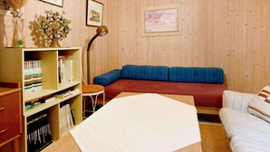 A cozy room with a wooden paneled wall, a blue sofa, a small table with a lamp, and a bookshelf filled with books. - 4 Person Holiday Home in Lysekil-by Traum (Lysekil)
