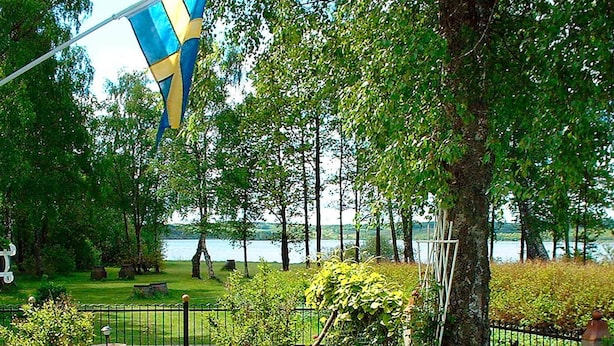 Un parque con vista a un lago, una bandera y un área cercada con bancos.