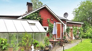 Una casa roja con un invernadero, una terraza de madera y plantas en macetas.