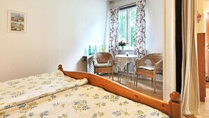 Un dormitorio con una cama de madera, una pequeña mesa con sillas y una ventana con cortinas florales.