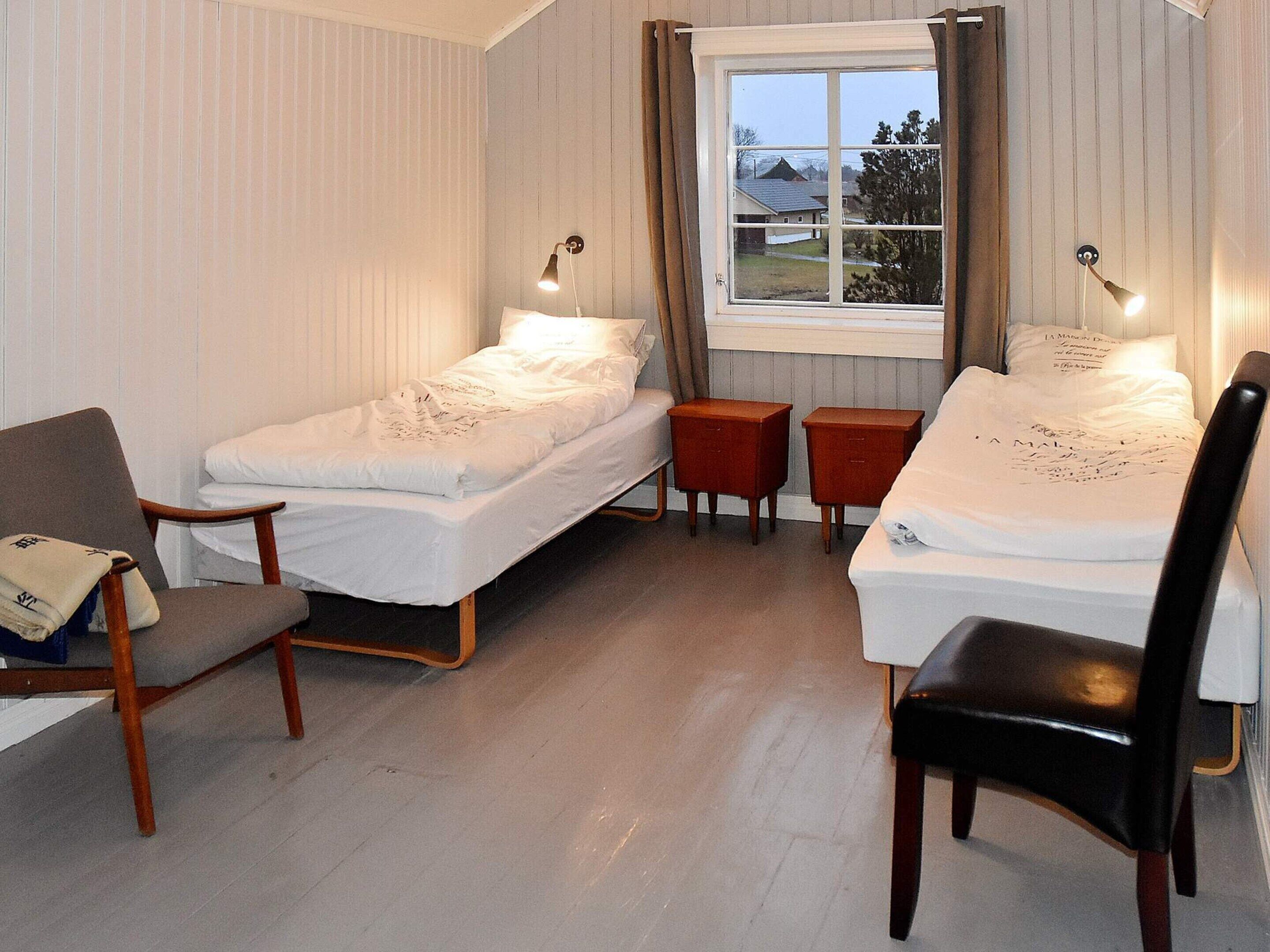 A room with two single beds, a wooden chair, a small table, and a window with curtains.