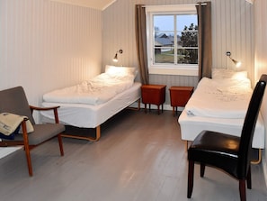 Een kamer met twee eenpersoonsbedden, een houten stoel, een tafeltje en een raam met gordijnen.