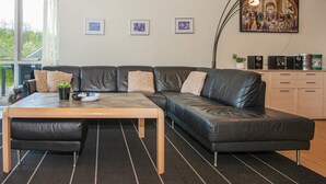 A modern living room with a leather sofa, a wooden coffee table, and a black rug. There are framed pictures on the wall and a large painting above the sofa.