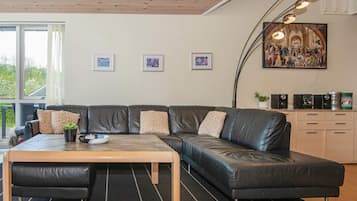 A modern living room with a leather sofa, a wooden coffee table, and a black rug. There are framed pictures on the wall and a large painting above the sofa.