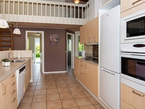 A modern kitchen with a built-in oven, a microwave, and a sink. There is a wooden ceiling and a view of the outdoors. - 4 Star Holiday Home in Aabenraa (Aabenraa)