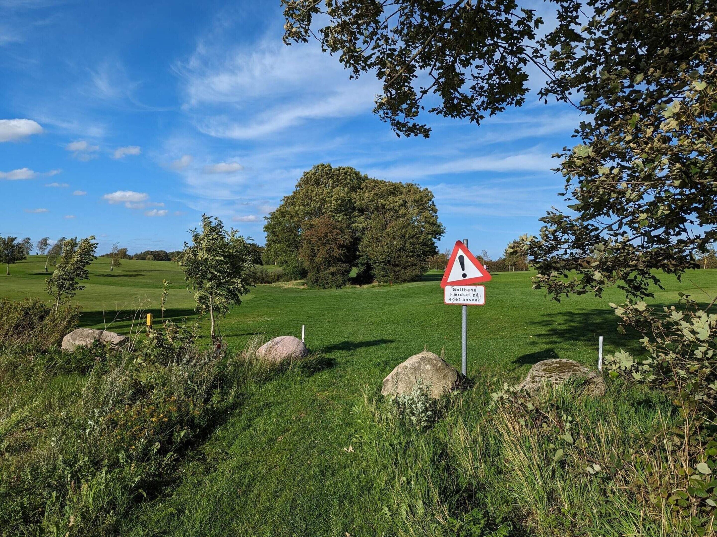 A golf course with a warning sign, trees, and a clear blue sky.