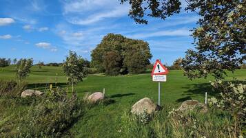 A golf course with a warning sign, trees, and a clear blue sky.