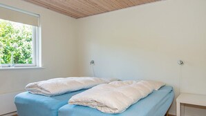 A room with two beds, a window with a view of greenery, and a wooden ceiling.