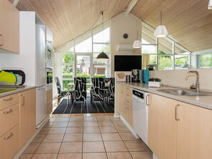 A modern kitchen with wooden cabinets, a built-in dishwasher, and a large window providing natural light. - 4 Star Holiday Home in Aabenraa (Aabenraa)