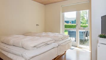 Quarto com cama de casal, mesa de cabeceira, televisão e porta de vidro corrediça que dá para uma área externa.