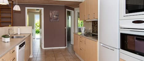 A kitchen with a built-in oven, a microwave, and a sink. There is a wooden ceiling and a view of the outdoors.