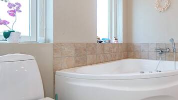 Un baño con una bañera blanca, un inodoro y una ventana con vistas al exterior.