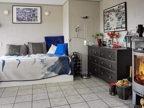 A bedroom with a bed, a dresser, a floor lamp, a fireplace, and a wall with framed photos.