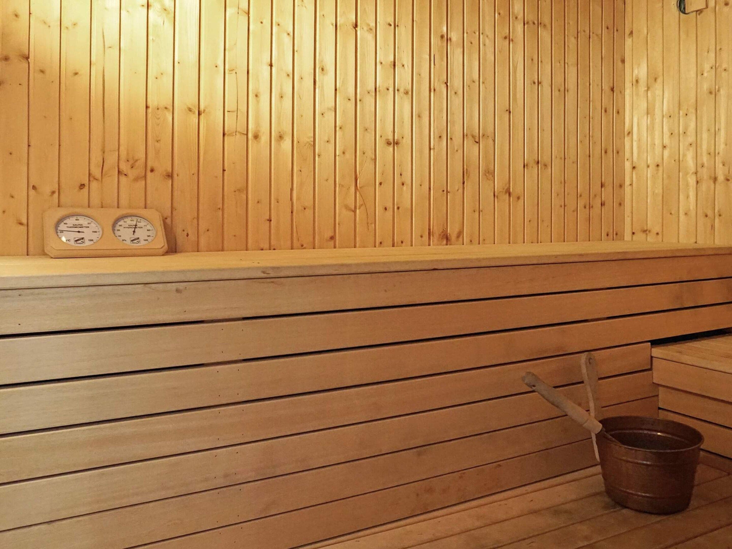A sauna with wooden walls and benches, a thermometer, and a bucket on the floor.