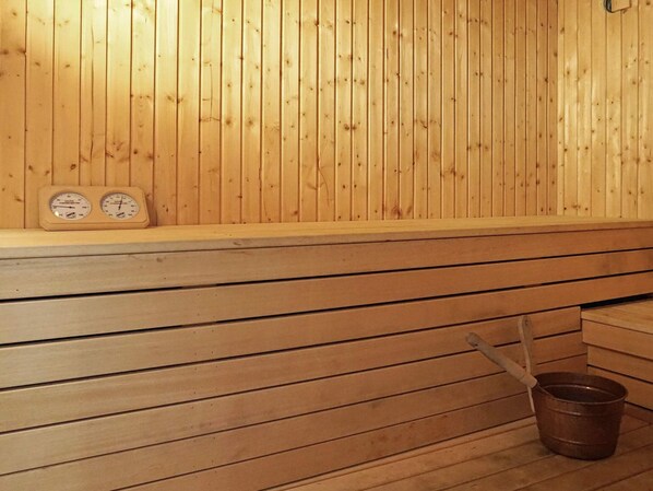 A sauna with wooden walls and benches, a thermometer, and a bucket on the floor.