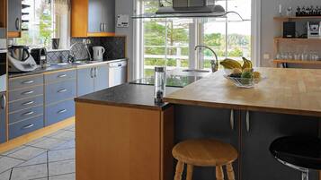 A modern kitchen with grey cabinets, a wooden countertop, a built-in stove, and a window with a view of greenery.