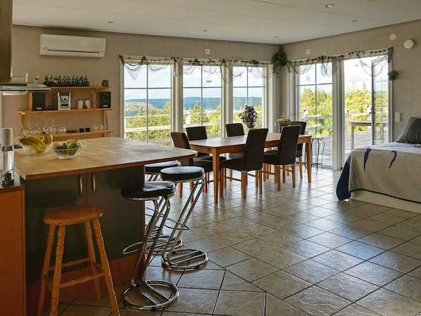 A modern kitchen with a large island, bar stools, and a dining area with chairs. There are large windows with a view of the outdoors. - Holiday Home in HenÃ¥n (Henån)
